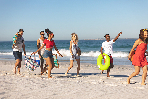 Front view of group of happy diverse friends walking together on the beach