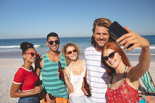 Front view of group of young diverse friends taking selfie with mobile phone on the beach