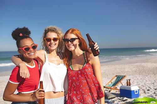 Front view of group of young diverse female friends standing together on the beach