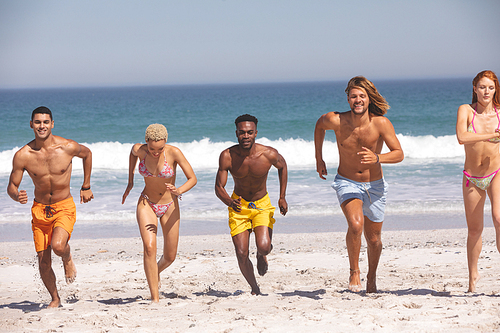Front view of group of young diverse friends running together on the beach