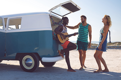 Side view of happy group of diverse friends having fun together near camper van at beach