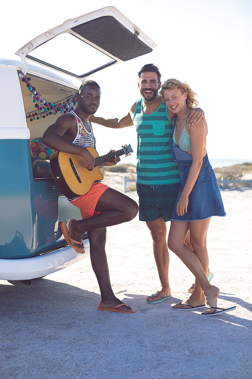 Front view of happy group of diverse friends having fun together near camper van at beach