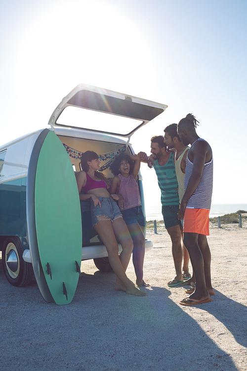 Front view of young group of diverse friends interacting with each other near camper van at beach