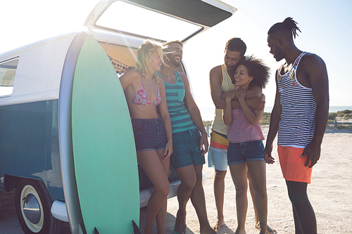 Front view of young group of diverse friends interacting with each other near camper van at beach