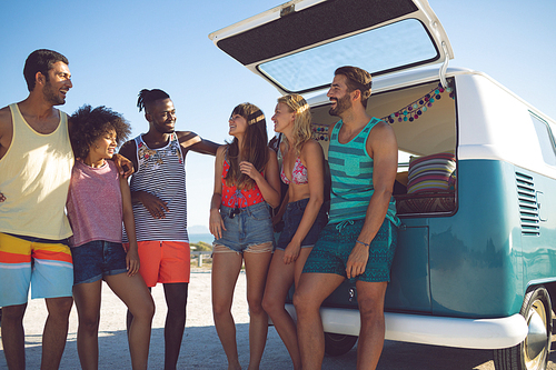 Front view of happy group of diverse friends interacting with each other near camper van at beach