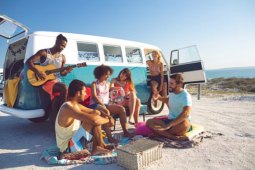 Side view of young group of diverse friends having fun near camper van at beach