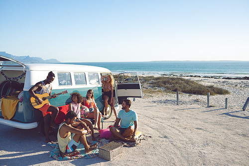 Front view of young group of diverse friends having fun near camper van at beach