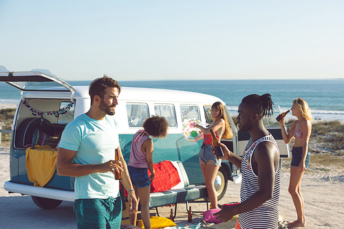 Side view of young group of diverse friends having fun near camper van at beach
