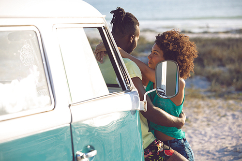 Side view of romantic mixed race couple embracing each other near camper van at beach