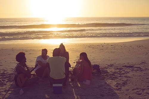 Rear view of young group of diverse friends having fun at beach during sunset