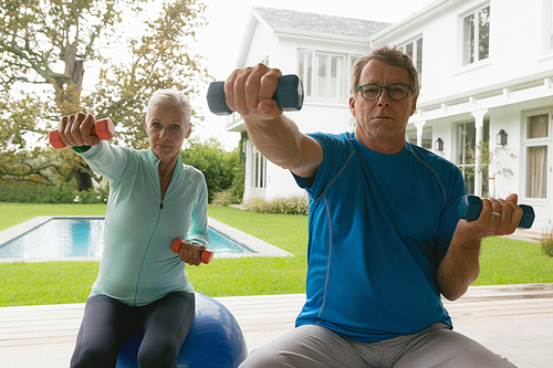 Front view of active senior Caucasian couple exercising with dumbbell in porch at home