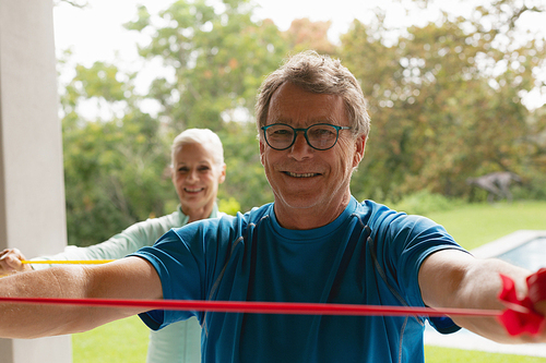 Front view of active senior Caucasian couple exercising with resistance band in porch at home