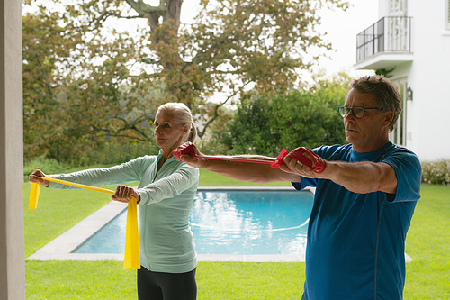 Side view of active senior Caucasian couple exercising with resistance band in porch at home