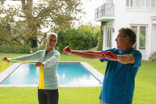 Side view of happy active senior Caucasian couple exercising with resistance band in porch at home