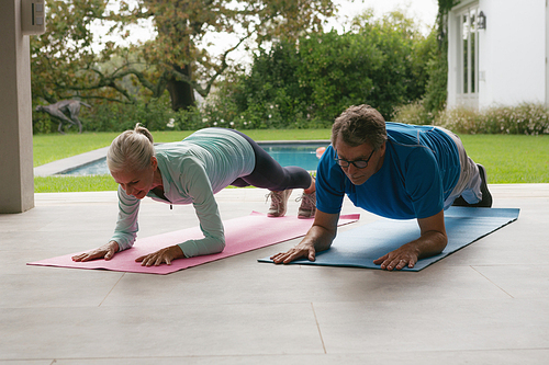 Front view of determined active senior Caucasian couple doing plank exercise in the porch at home