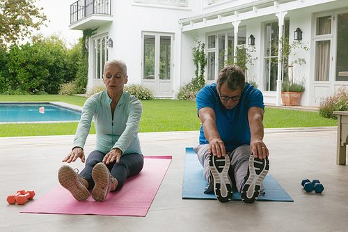 Front view of determined active senior Caucasian couple doing stretching exercise in the porch at home