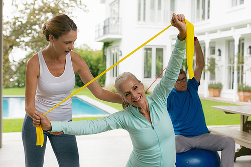 Front view of Caucasian female trainer assisting active senior couple to exercise with resistance band in the porch at home