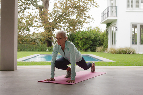 Front view of determined active senior Caucasian woman doing yoga on exercise mat in the porch at home