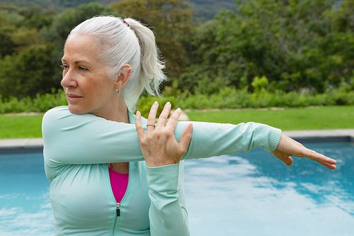 Side view of active senior Caucasian woman exercising near poolside in the backyard of home