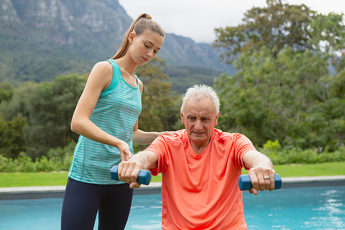 Front view of Caucasian female trainer assisting active senior man to exercise with dumbbells in the backyard