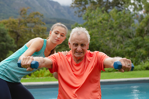 Front view of Caucasian female trainer assisting active senior man to exercise with dumbbells in the backyard