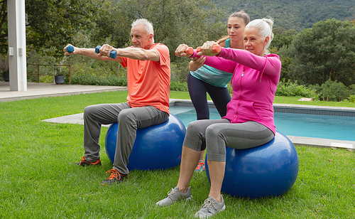Side view of Caucasian female trainer assisting active senior Caucasian couple to exercise with dumbbells in the backyard