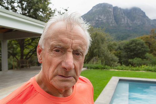 Portrait of active senior Caucasian man standing with exercise mat near poolside in the backyard