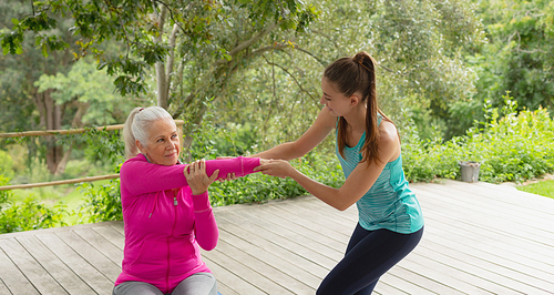 Side view of beautiful Caucasian female trainer assisting active senior Caucasian woman to exercise in the porch