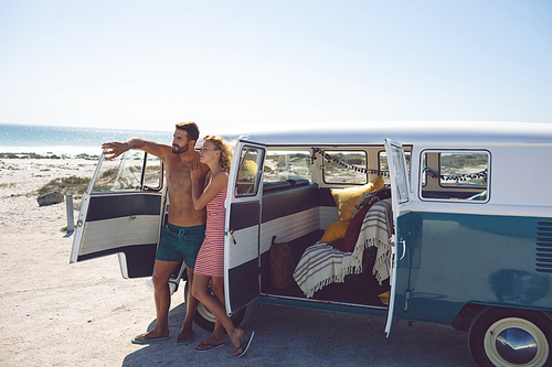 Front view of young Caucasian couple standing near camper van at beach in the sunshine