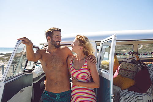 Front view of happy Caucasian couple talking with each other near camper van at beach in the sunshine