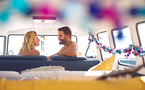 Rear view of happy Caucasian couple talking with each other in camper van at beach