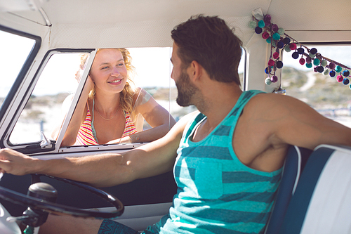 Side view of Caucasian man in camper van talking with woman while woman standing outside the van at beach