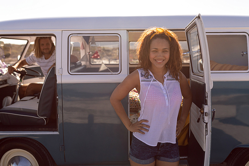 Front view of happy Mixed-race woman with hands on hip standing near camper van at beach