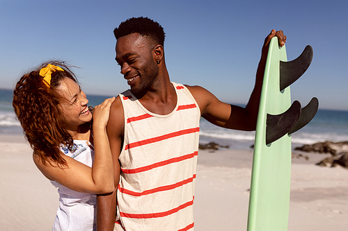 Front view of happy young Mixed-race couple with surfboard looking each other on beach in the sunshine
