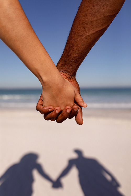 Close-up of Mixed-race couple holding hands on beach in the sunshine