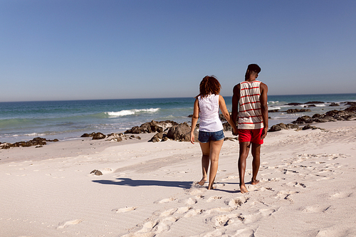 Rear view of Mixed-race couple holding hands and walking on beach in the sunshine