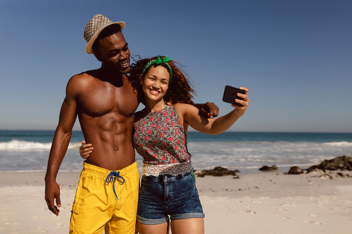 Front view of happy young Mixed-race couple taking selfie with mobile phone on beach in the sunshine
