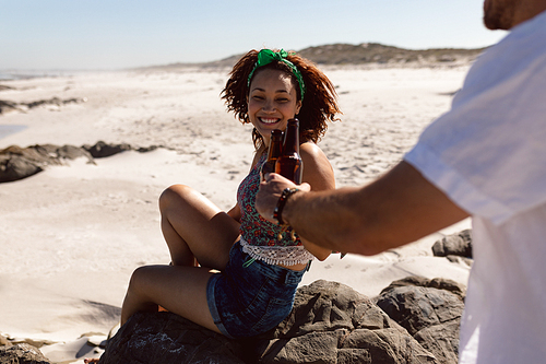 Rear view of happy young Mixed-race couple toasting beer bottle on beach in the sunshine