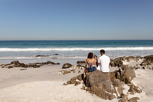 Rear view of young Mixed-race couple toasting beer bottle on beach in the sunshine