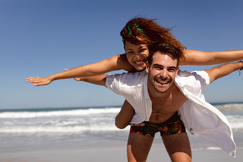 Front view of happy Mixed-race man giving piggyback to woman on beach in the sunshine