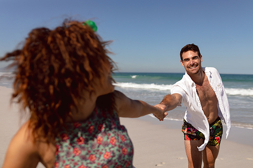 Front view of happy young Mixed-race couple holding hands on beach in the sunshine