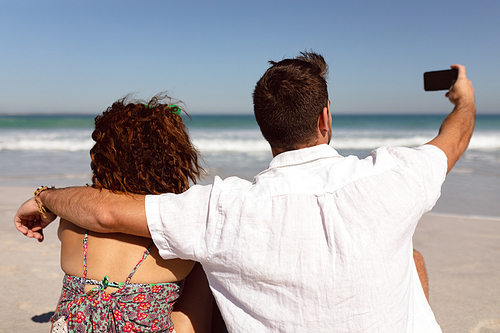 Rear view of Mixed-race couple taking selfie with mobile phone on beach in the sunshine