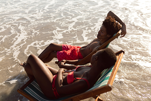 High angle view of African-american couple interacting with each other while relaxing in a beach chair on the beach