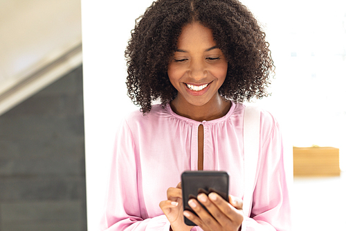 Front view of young pretty African-american employee looking her phone in modern office