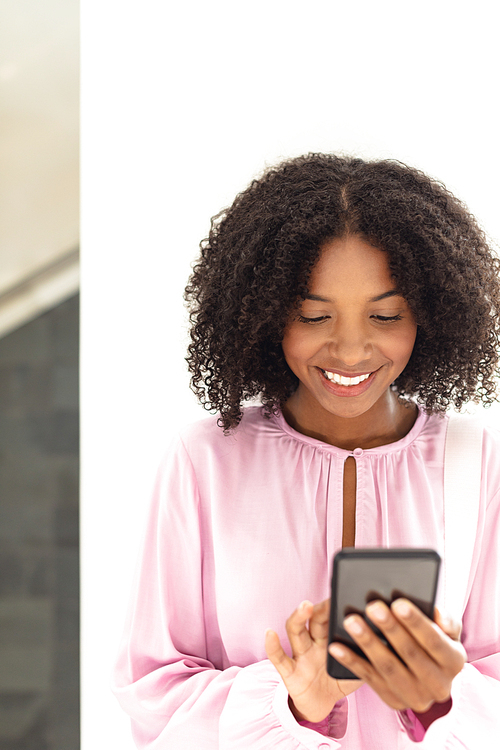 Front view of young pretty African-american employee looking her phone in modern office