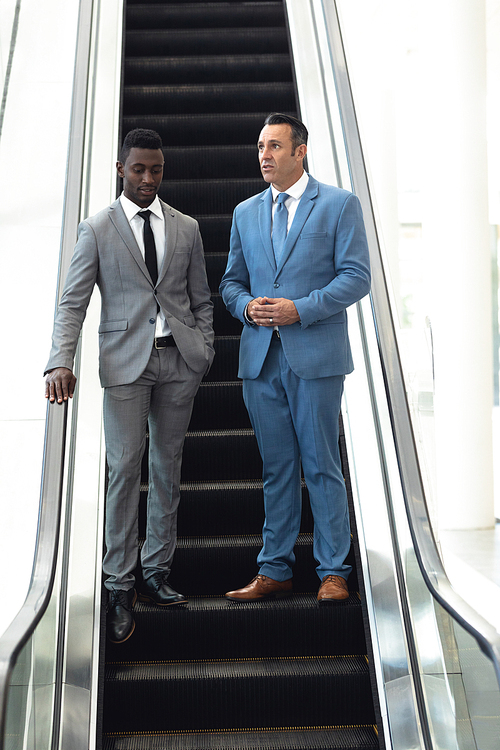 Front view of African-american young male executive talking with mature male executive in escalator