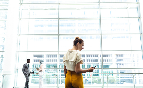 Rear view of young female executive looking at her mobile phone in modern office