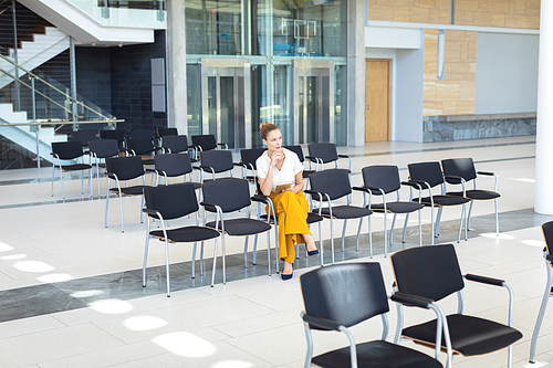 Front view of young Caucasian female executive looking away while sitting on chair in empty conference room