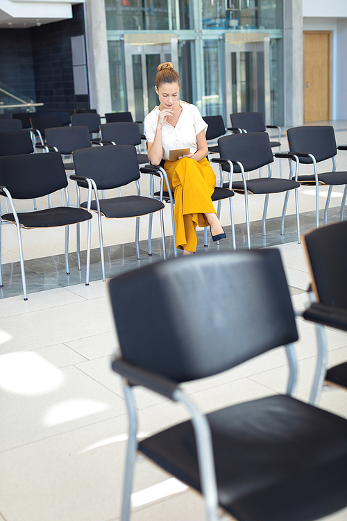 Front view of young Caucasian female executive looking at digital tablet while sitting on chair in empty conference room