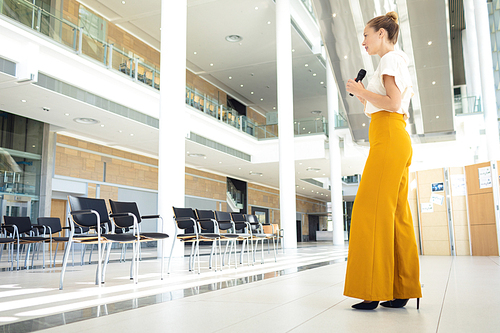 Low angle view of young Caucasian female executive standing with microphone while looking at empty conference room